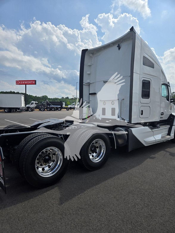 Kenworth T680 conventional sleeper truck in a dealership lot, rear cab area visible, dual rear axles, polished chrome wheels, white exterior.