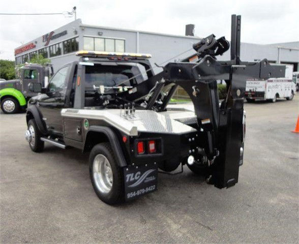Tow truck chassis with a hydraulic boom and winch, RAM 4500 SLT front cab, metal diamond plate step panels, rear wheel, tow equipment in middle, and warning lights on top.