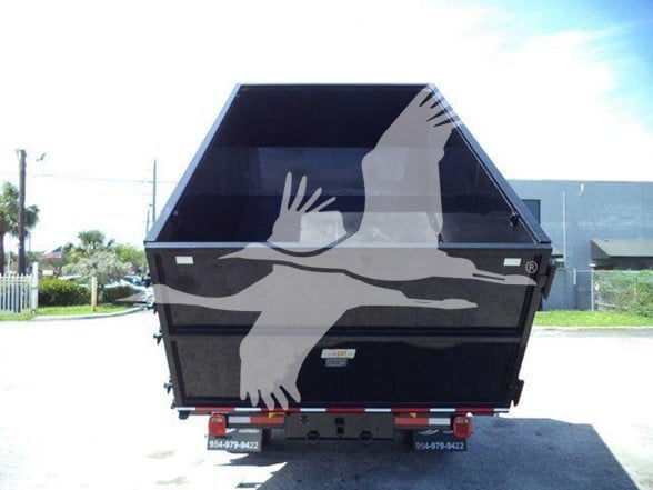 Back of a black dump trailer in a dealership lot with a large graphic of hands reaching upward and a bird, license plate area at bottom.