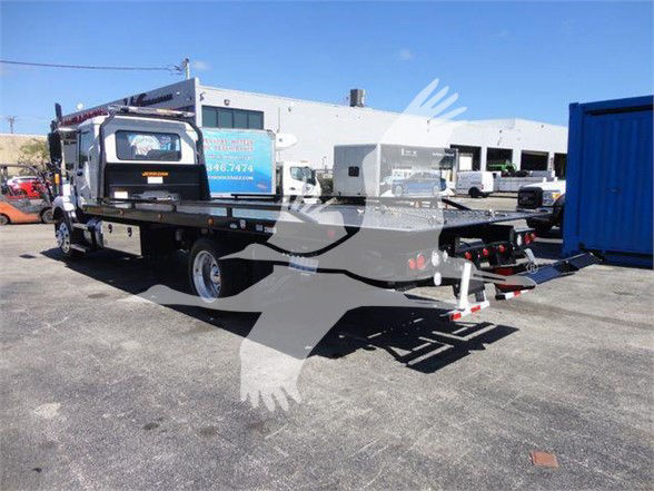 2024 Mack MD6 tow truck in a parking lot with a trailer; side view shows cab, flatbed, and hitch components.