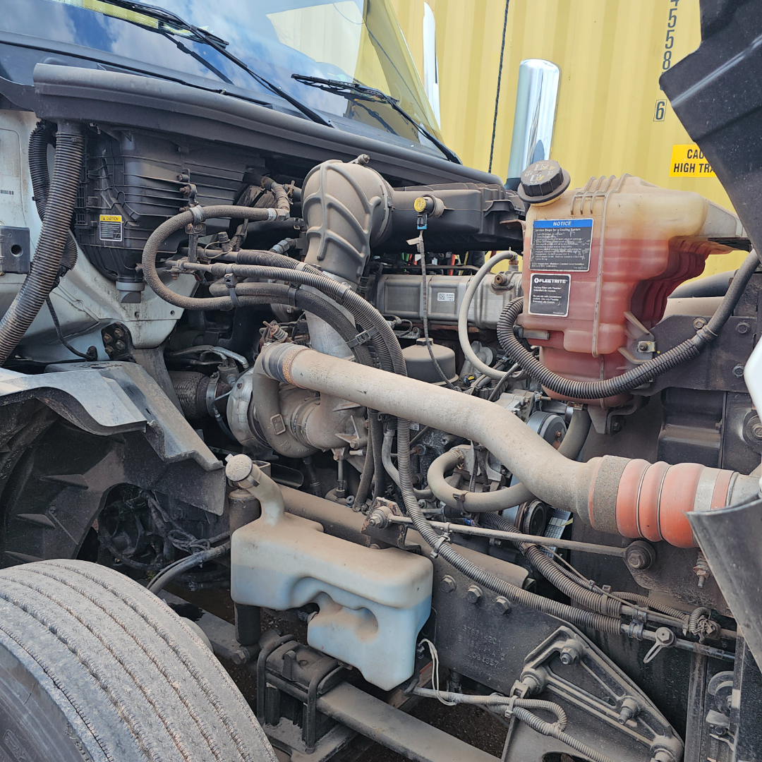 Image of a truck engine bay showing radiator reservoir, coolant bottle, hoses, air intake, and battery area.