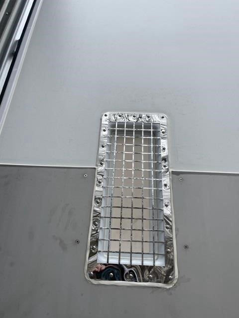 Reefer trailer roof vent or access hatch with metal mesh grill and fasteners, on a light gray surface.