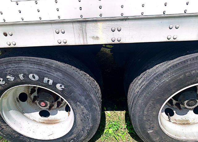 Dual rear wheels of a Vanguard VXP trailer with silver riveted aluminum side panel above and white wheels. Visible tires show tread and rims.