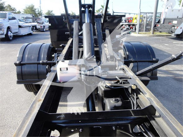Truck chassis with dual rear axles and hydraulic components visible in foreground.
