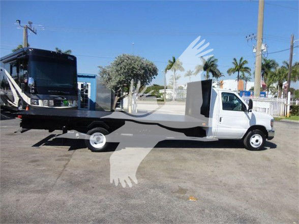 Flatbed tow truck with white cab and long black flatbed, Ford E-450 chassis, side view showing wheel hubs and rear equipment.
