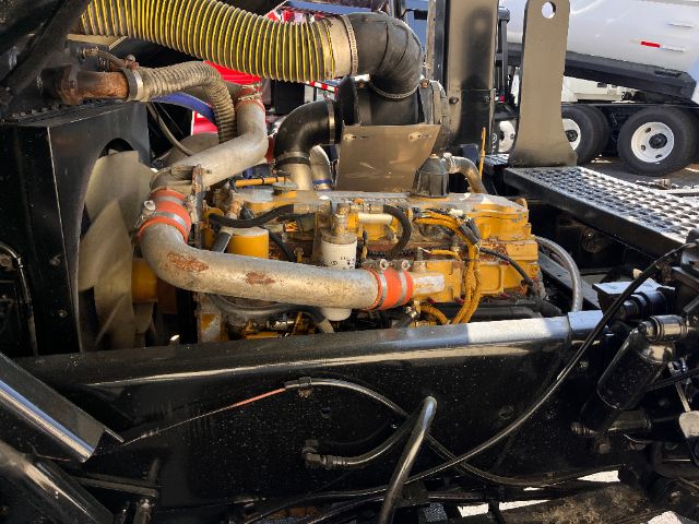 Industrial diesel engine bay of a Kalmar Ottawa 30 yard truck showing yellow engine components, hoses, and coolant pipes.