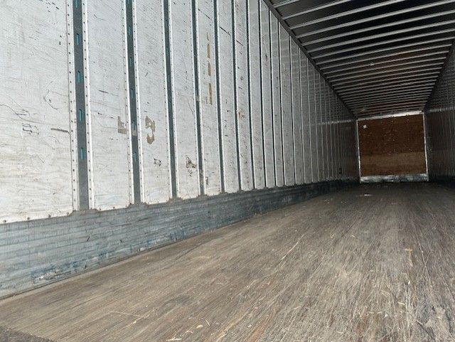 Trailer interior showing wooden floor and ribbed metal side walls with door at far end