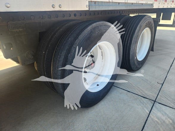 Dual rear trailer wheels under a Stoughton van trailer with white rims and black tires. VIN and stock info visible in listing area above.