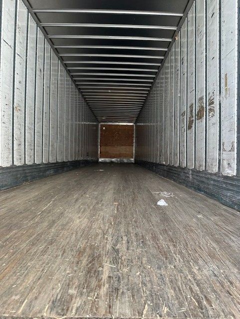Inside a long empty trailer with wooden floor and aluminum side walls, viewed from near the back, showing a closed rear door.
