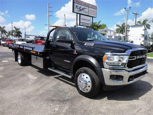 Ram 5500 SLT tow truck with a flatbed, black cab and chrome front grille, side view showing dual rear wheels and extended flatbed.