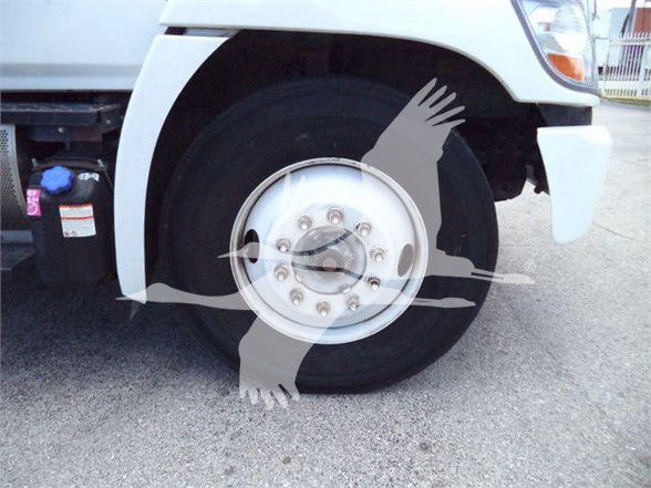 Truck front wheel and fender with hubcap, white body, no text visible on wheel; partial view of undercarriage and bumper.