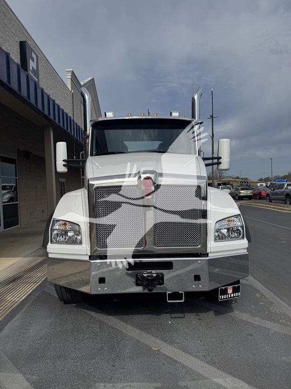 Kenworth T880 front view showing large chrome grille and bumper, white cab, dual vertical exhaust stacks, and truck emblem on grille.