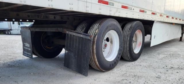 Trailer axle with dual tires and mud flaps under utility trailer showing wheel rims and tire details.