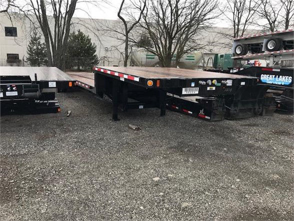Flatbed trailer in a lot, parked next to another trailer with a Great Lakes sign, painted black with red/white reflective striping along the edges.