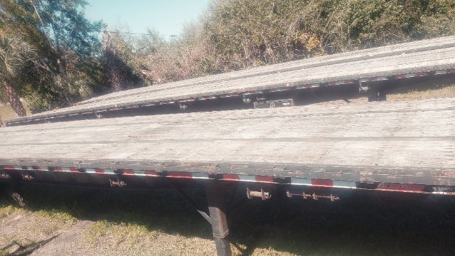 Flatbed trailer deck showing weathered wood planks and metal side rails; some reflective tape visible along edge.
