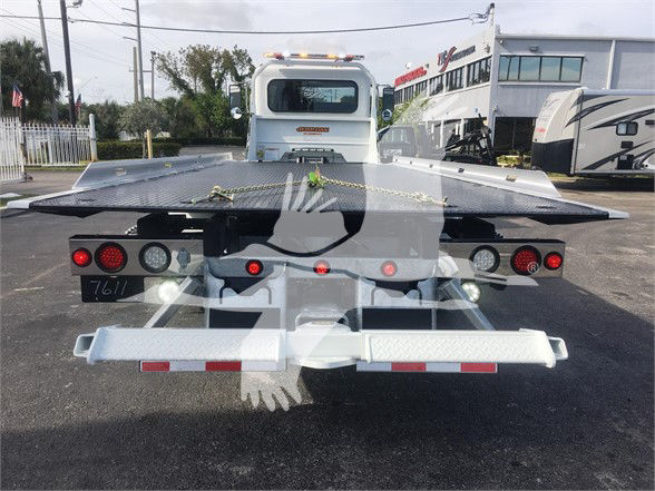 Peterbilt tow truck chassis shown from rear with a hydraulic tilt bed and multiple taillights, rear bumper, and deck plates. Visible stickers and chain securing the bed.