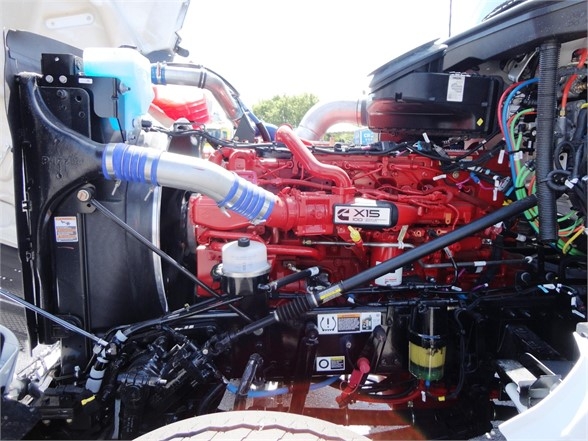 Kenworth W990 engine bay with red engine labeled X15, various hoses, coolant reservoir, and wiring harnesses visible.