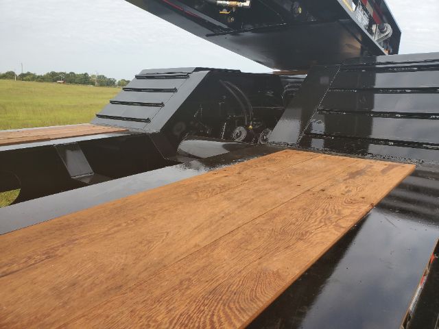 Lowboy trailer bed with wooden planks and hydraulic mechanism visible under a raised section.