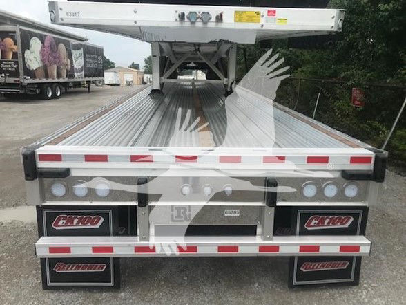Rear view of a new 2026 Reitnouer CK 100 flatbed trailer showing reflective red/white safety stripes, cargo deck, taillights, and mud flaps with Reitnouer logo.