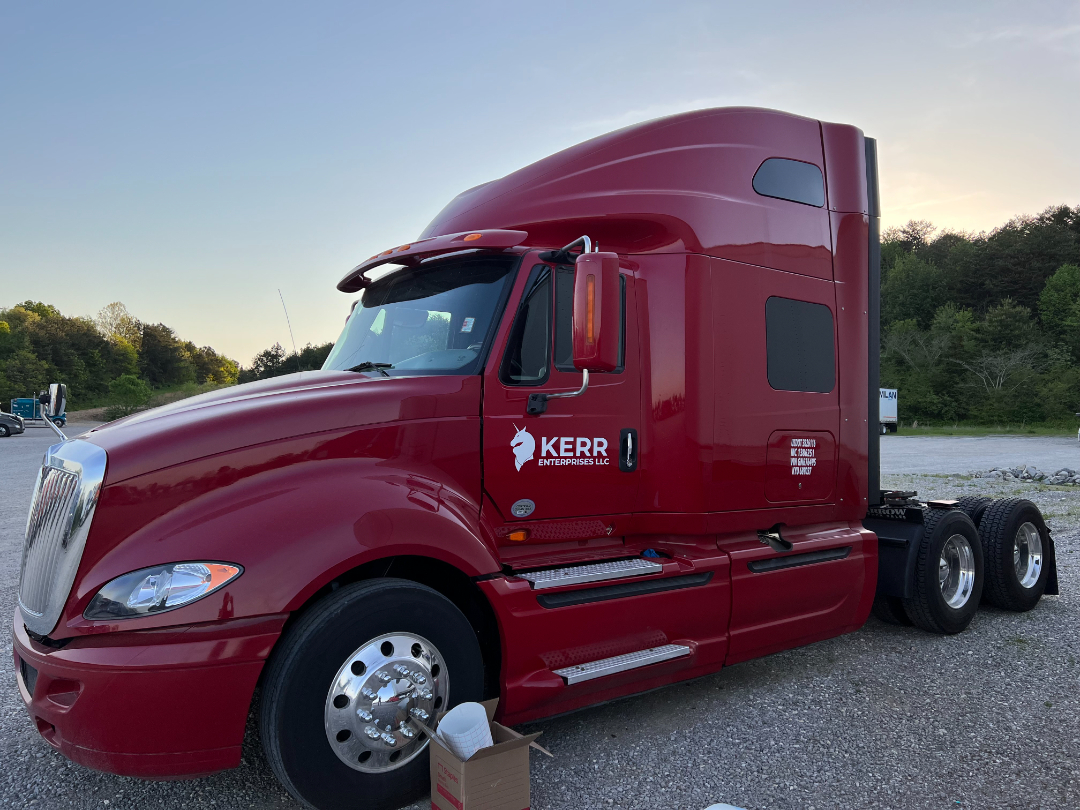 Red 2016 International Prostar truck with Kerr Enterprises LLC branding, sleeper cab, side view showing front wheel, chrome hubcap, and dual rear axles.