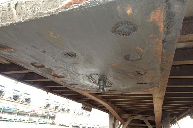 Underbelly of a curtain-side trailer showing a hitch/bolt arrangement and rust spots on the metal plate.