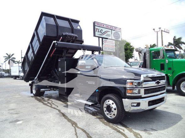 2023 Chevrolet Silverado 6500HD dump truck in driveway showing raised dump bed and hydraulic cylinders with front chrome bumper and Chevrolet emblem.