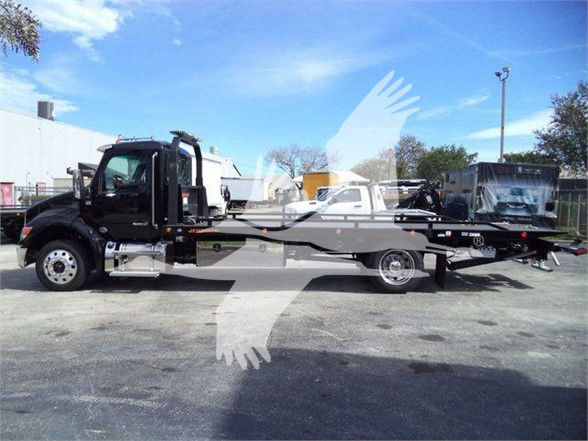 Kenworth T880 or similar cab-over tow truck chassis in a parking lot, long wheelbase with flatbed and crane area visible.