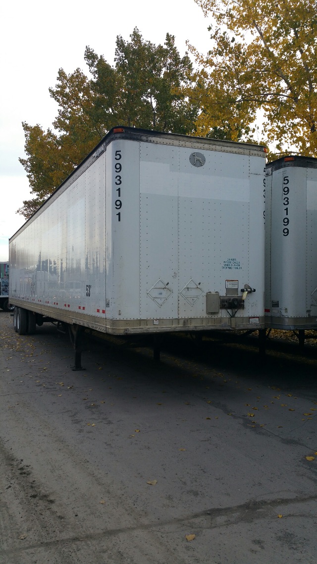 Rear view of a white 2003 Great Dane 53ft dry van trailer with black ID numbers on the left rear corner and two diamond placards. Lifting legs and undercarriage visible.