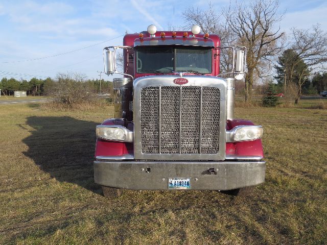 Peterbilt 388 truck front view with chrome grille, maroon cab, large bumper, and two round mirrors. License plate visible on bumper.