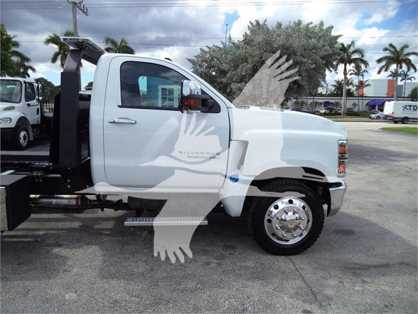 Side view of a white 2023 Chevrolet Silverado 6500HD tow truck chassis. Visible text on door: 'CHEVROLET' and some emblem. No other legible labels or serials visible in image.
