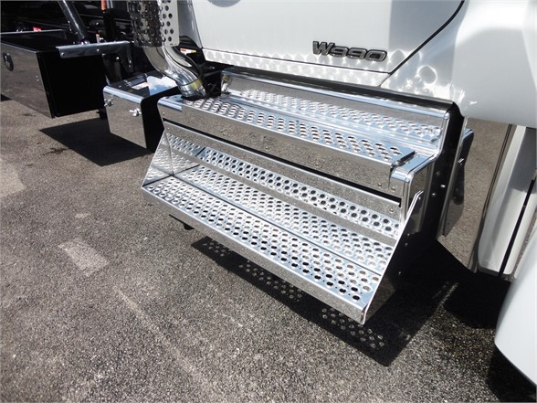 Kenworth W990 side view showing polished chrome aluminum fold-out running board beneath cab step area.