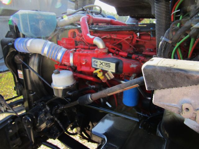 Kenworth T680 engine bay with red XR15 badge, blue coolant reservoir hose, white filter canister, and various hoses and wiring.