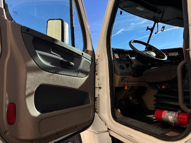Truck cab interior showing open door, steering wheel, and driver's seat in a Freightliner Cascadia cab.