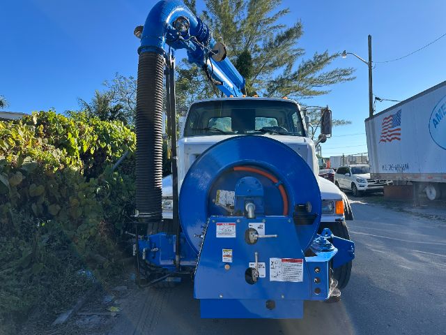 Blue vacuum truck with reel and hose mounted on rear, Sterling L7500 cab visible, white cab, blue body equipment, hydraulic exhaust/boom assembly in yard.