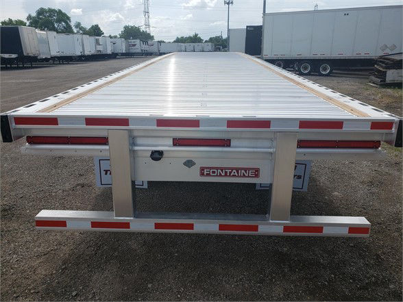 Flatbed trailer bed with Fontaine logo on rear, aluminum deck and side rails, rear bumper and safety reflectors visible in a truck yard.