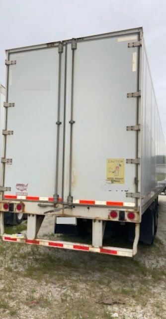 Rear of a white trailer with double doors, safety decals, and red reflective tape along the bumper.
