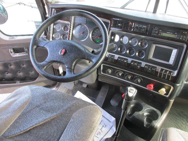 Kenworth W900 truck interior showing steering wheel, gauge cluster, and center console with multiple controls and gear shifter.