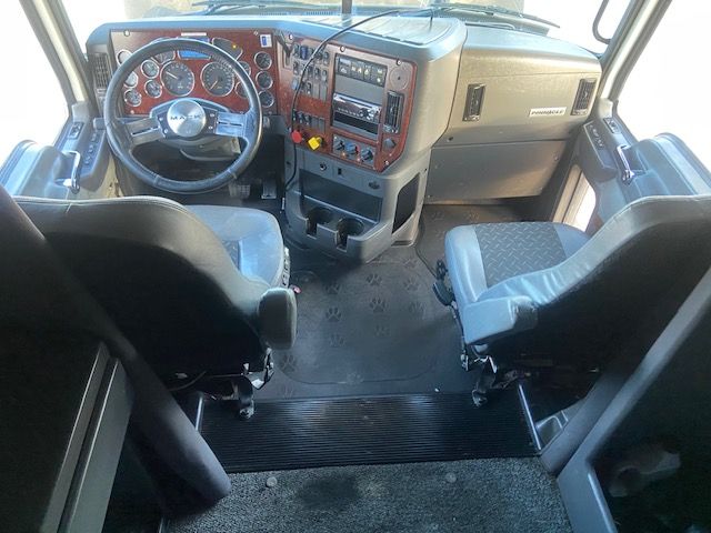 Truck cab interior showing steering wheel dashboard gear shifter and two seats in a Mack CXU613 cockpit.