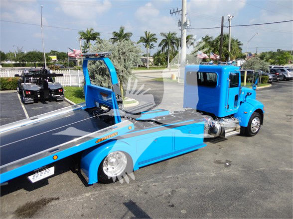 Blue Peterbilt 337 tow truck with flatbed, side view shows low-profile deck and cab. Stock tag J56606.