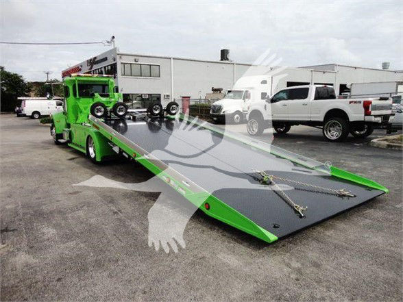 Peterbilt 337 tow truck with a bright green tow bed, flatbed ramp extended in a parking lot.
