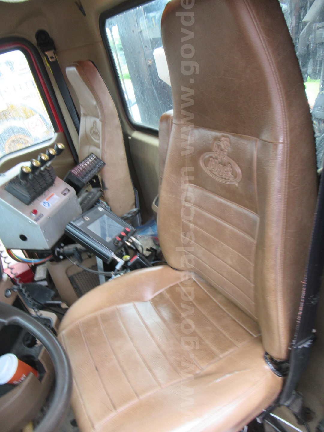 Cab interior of a Mack GU713 truck showing brown leather seat, control panel with switches and a mounted screen, and a console with wiring.
