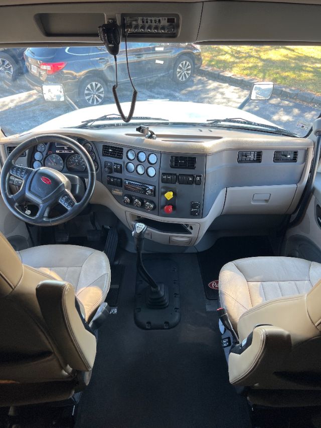 Truck cab interior of a 2018 Peterbilt 579 with steering wheel, dashboard controls, gear shifter, and two front seats.