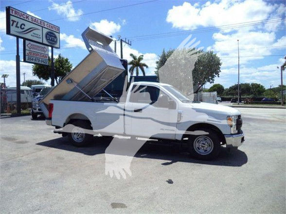 Ford F-250 dump truck with bed raised showing cargo area and cab in a dealership lot.