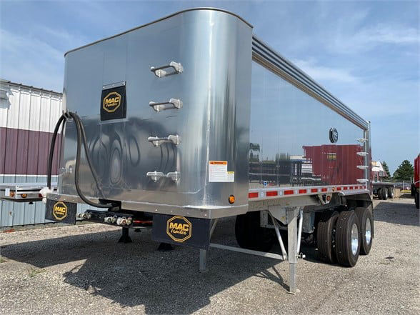 Utility aluminum dump trailer with top hinge door, dual rear axles, and MAC Trailers logo on front corner. Side panels reflective, front jack and hitch visible.