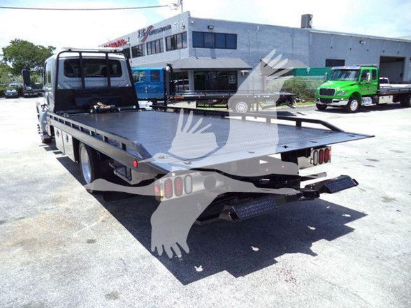 Flatbed tow truck in yard with other trucks, rear platform visible.