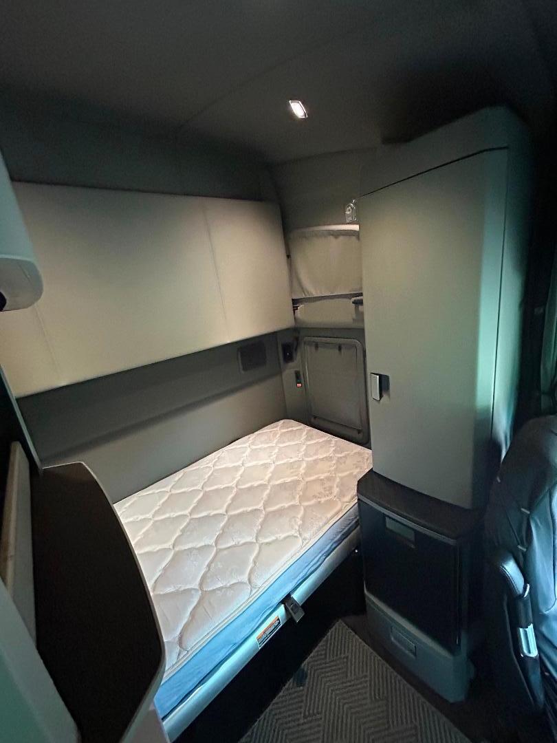 Truck sleeper cab interior with single bunk and mattress in a 2020 Kenworth T680. Side storage cabinets and door panel visible.