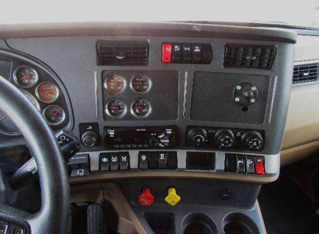 Truck cab interior dashboard showing multiple analog gauges, control switches, and two colorful knobs (red and yellow) below.