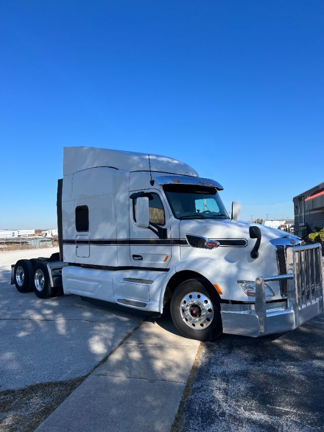 Truck cab showing Peterbilt 579 with chrome bumper and sleeper cab, front view on a clear day.