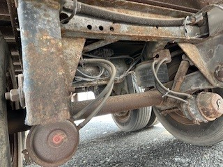 Trailer undercarriage showing suspension and hoses with circular air reservoir and rusted frame.