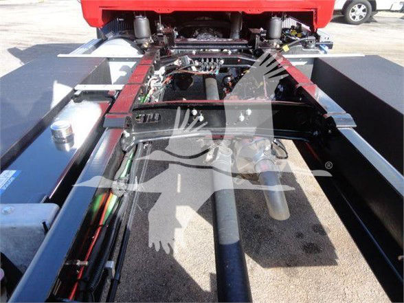 Mack MD6 chassis view with hydraulic lines and connectors visible under a red cab; machinery and frame components seen along the truck’s undercarriage.
